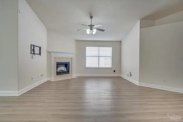 an empty room with wooden floor chandelier fan and windows