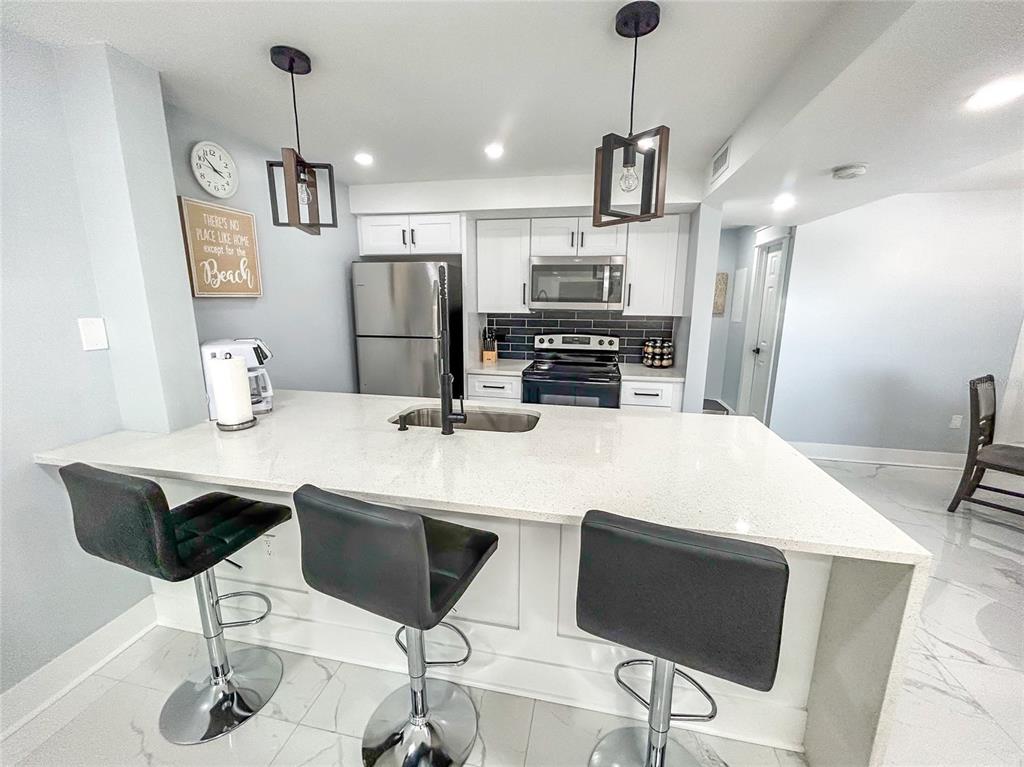 315 Medallion Boulevard, Unit F Madeira Beach, FL 33708 - Photo 4 of 18 a kitchen with stainless steel appliances kitchen island granite countertop a sink a microwave a refrigerator and chairs