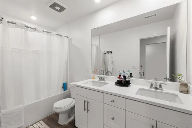 a bathroom with double sink a toilet a mirror and shower