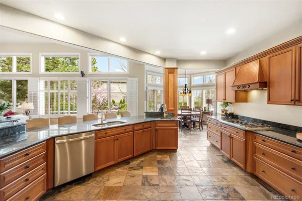 a large kitchen with stainless steel appliances granite countertop a stove top oven a sink dishwasher a dining table and chairs with wooden floor