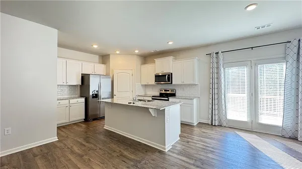 a kitchen with stainless steel appliances a refrigerator a sink dishwasher a stove top oven a refrigerator and white cabinets with wooden floor