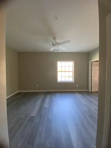 an empty room with wooden floor fan and windows