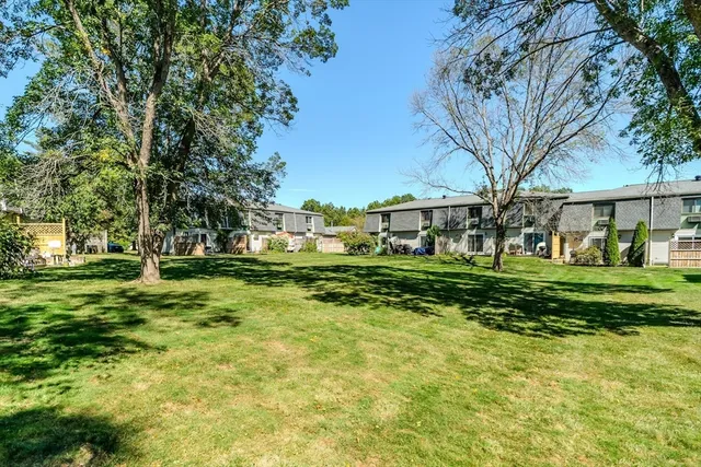 a view of a white house in front of a big yard with plants and large trees