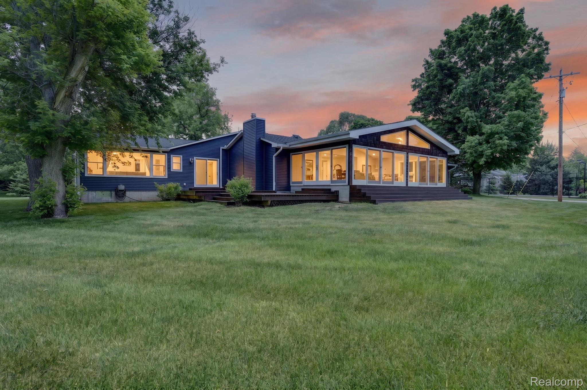 9353 Hill Road Swartz Creek, MI 48473 - Photo 4 of 98 Navy blue exterior with extensive glazing, a prominent chimney, a dark wood deck, and a sloping roofline