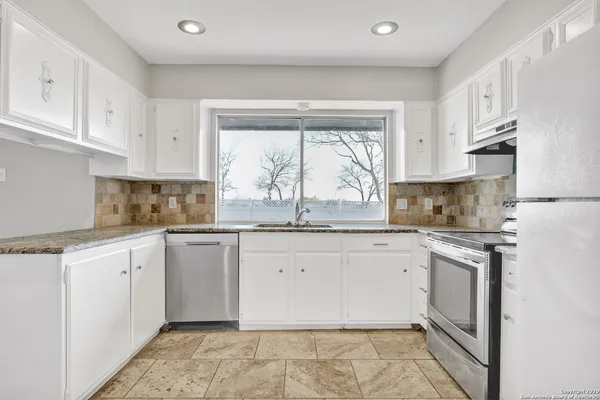 a kitchen with granite countertop white cabinets white appliances a sink and a window