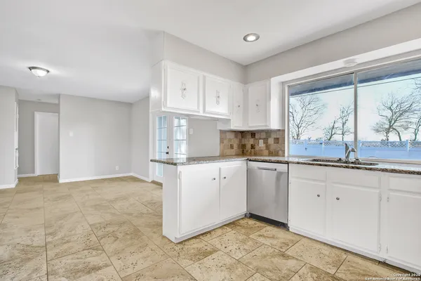 a kitchen with granite countertop white cabinets white appliances a sink and a large window