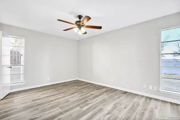 an empty room with wooden floor fan and windows