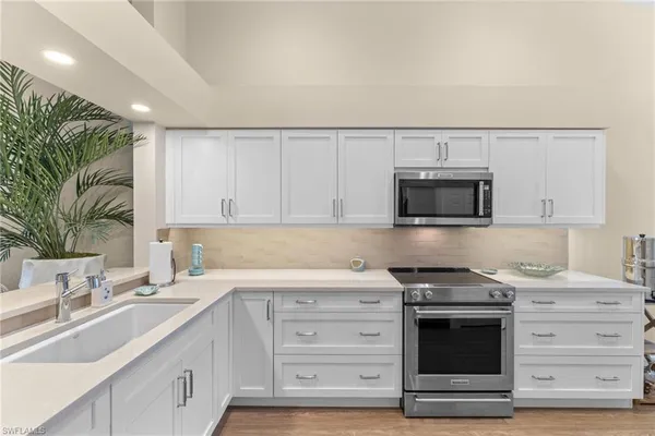 a kitchen with stainless steel appliances granite countertop a sink dishwasher a stove and a microwave oven with white cabinets