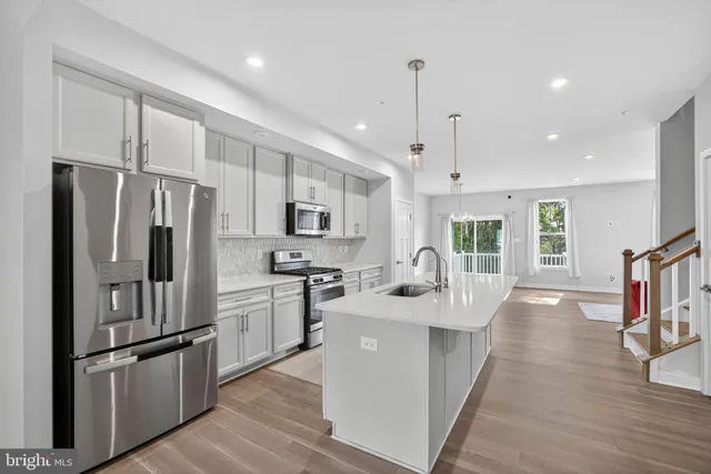 a kitchen with stainless steel appliances granite countertop a refrigerator a sink dishwasher a stove and white cabinets with wooden floor