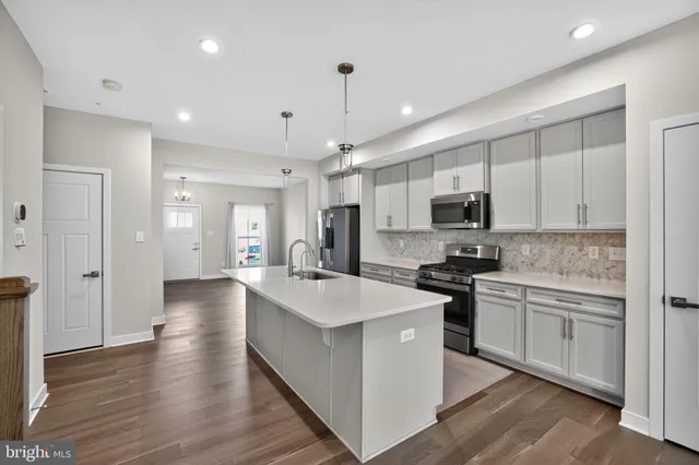 a large kitchen with stainless steel appliances kitchen island a stove a sink a refrigerator and white cabinets with wooden floor