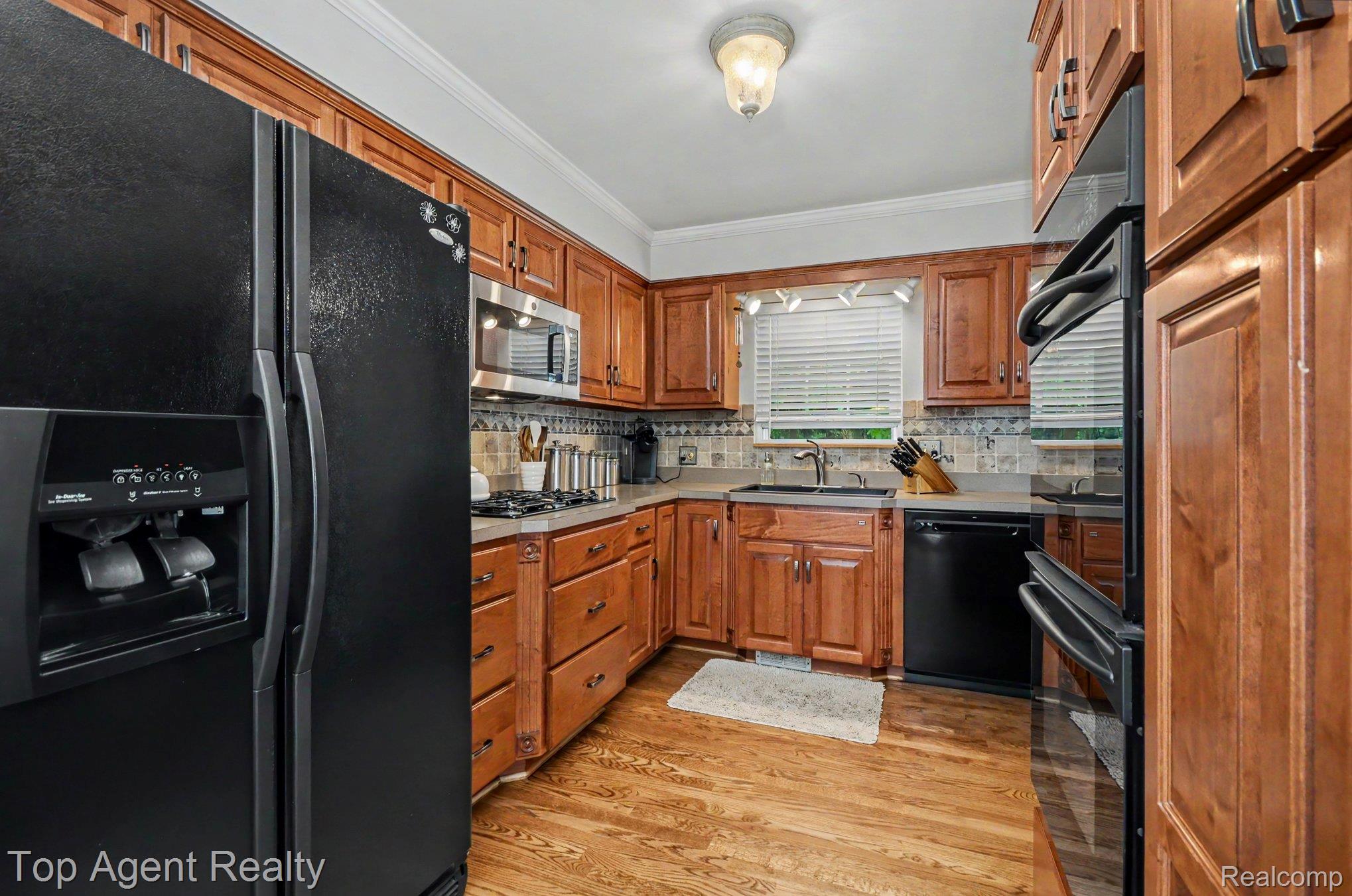 3759 Donley Avenue Rochester, MI 48309 - Photo 7 of 29 Kitchen featuring wood-finish flooring, warm-toned cabinetry, light-toned countertops, and black appliances