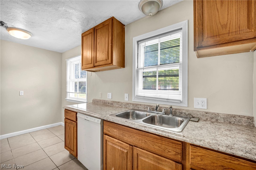 2313 North Taylor Road Cleveland Heights, OH 44112 - Photo 8 of 32 Kitchen featuring light wood cabinetry, laminate countertops with a built-in double basin stainless steel sink, a white dishwasher, and tile flooring