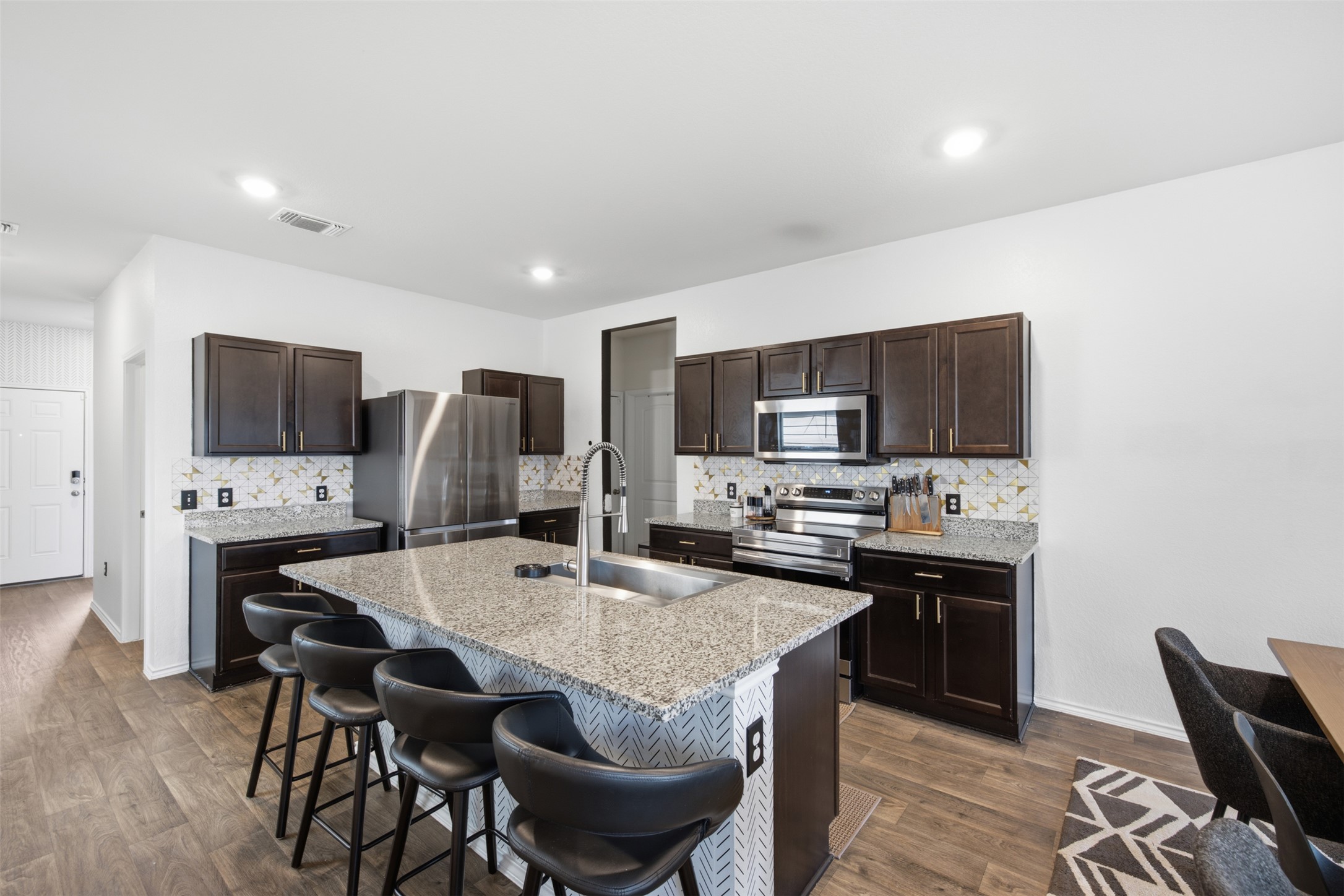 15000 Bajada Rd Manor Manor, TX 78653 - Photo 8 of 31 A contemporary kitchen features dark cabinetry, granite countertops, and stainless steel appliances, anchored by a spacious island with seating.