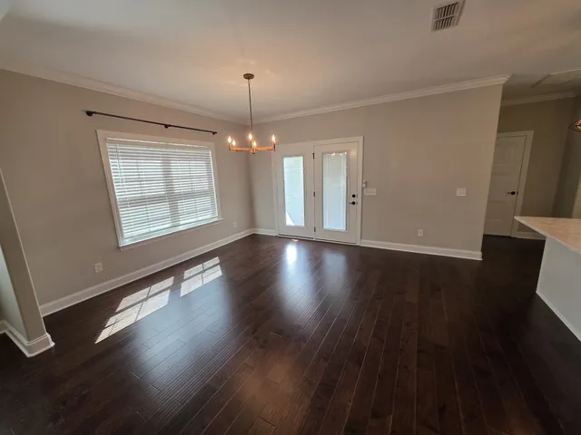 an empty room with wooden floor chandelier and windows