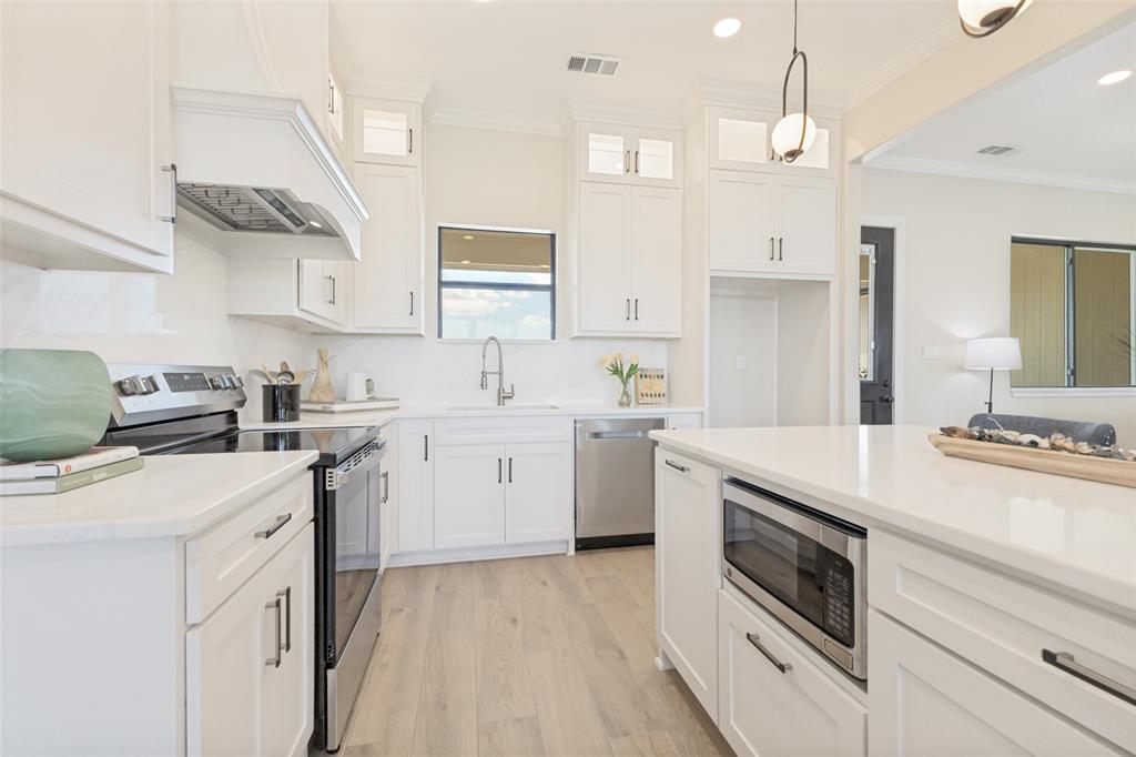 3150 Crisp Road Ennis, TX 75119 - Photo 8 of 30 Kitchen featuring white cabinetry, stainless steel appliances, a built-in microwave, light wood-finish flooring, and solid surface countertops