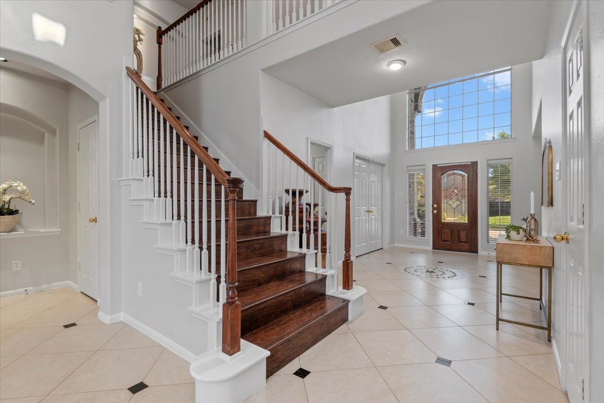 6507 Quiet Pointe Drive Spring, TX 77389 - Photo 18 of 46 This welcoming entryway features a high ceiling with abundant natural light from large windows. The elegant staircase has dark wooden steps. The space is complemented by neutral tile flooring and a stylish front door, creating a bright and inviting atmosphere.