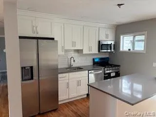 a kitchen with stainless steel appliances granite countertop a stove a refrigerator a sink and white cabinets