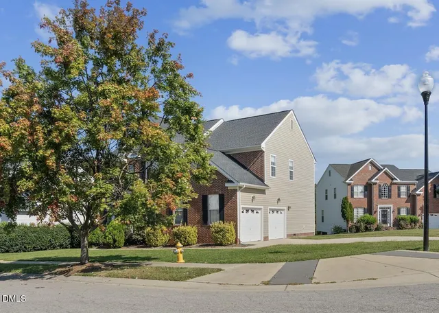 a view of a white house next to a yard with big trees