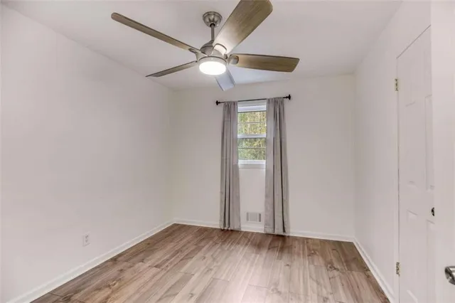 an empty room with wooden floor fan and windows