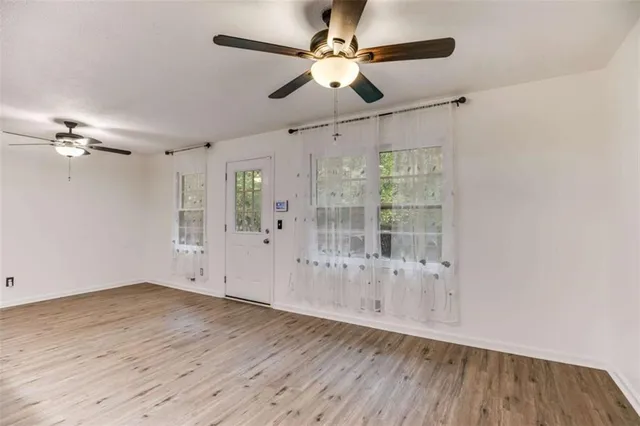 a view of an empty room with wooden floor and a ceiling fan