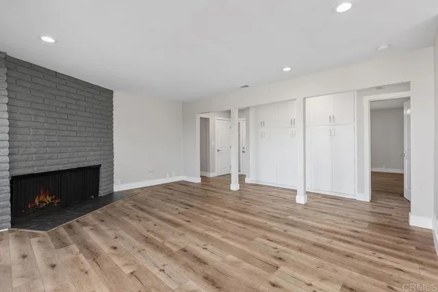 a view of an empty room with wooden floor fireplace and a window