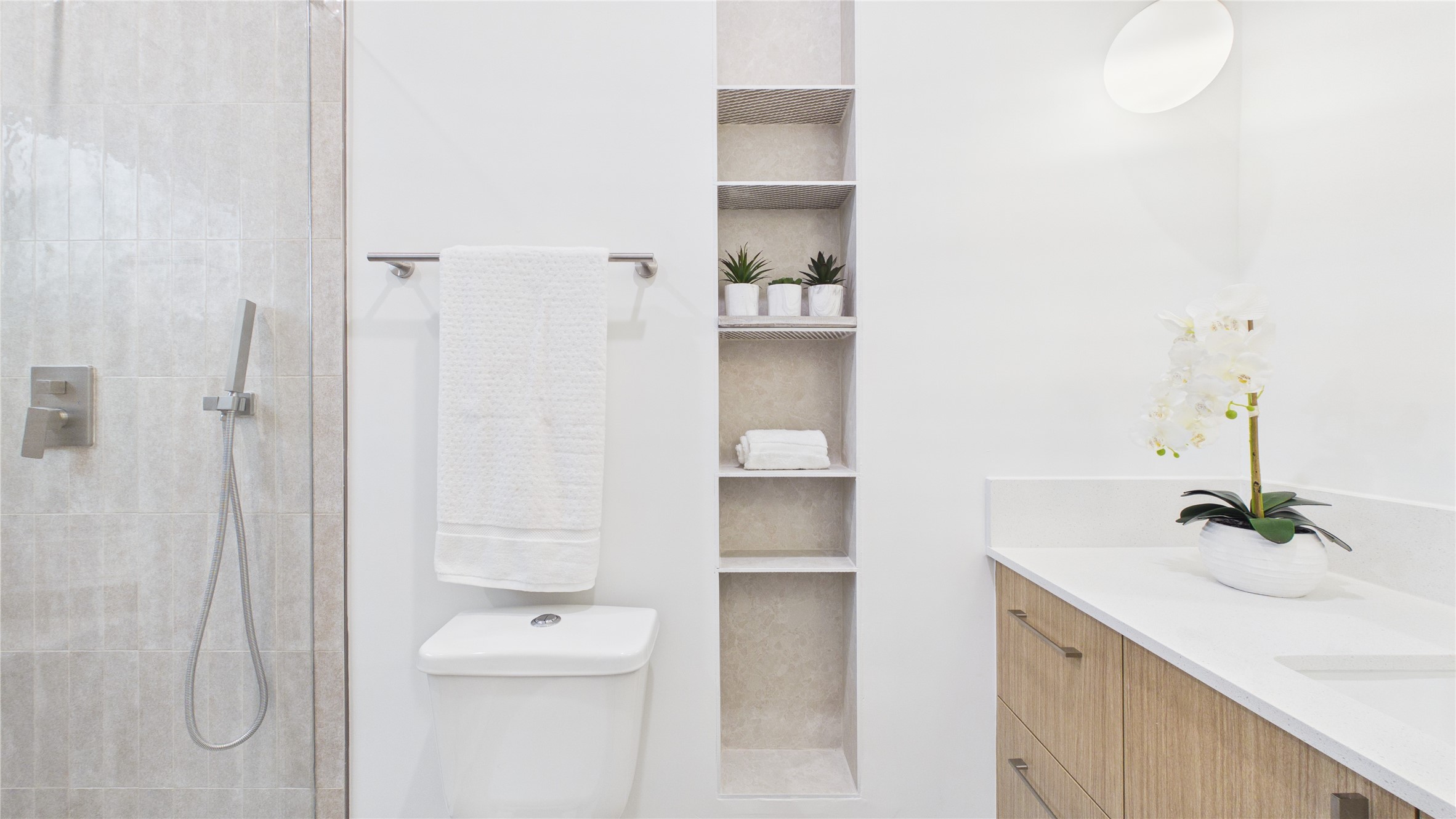 602 Skyland Terrace Way Houston, TX 77009 - Photo 11 of 40 This bathroom features a sleek design with a glass shower, modern fixtures, built-in shelving, and a wooden vanity with a white countertop. It's accented with potted plants and a decorative orchid for a touch of elegance.