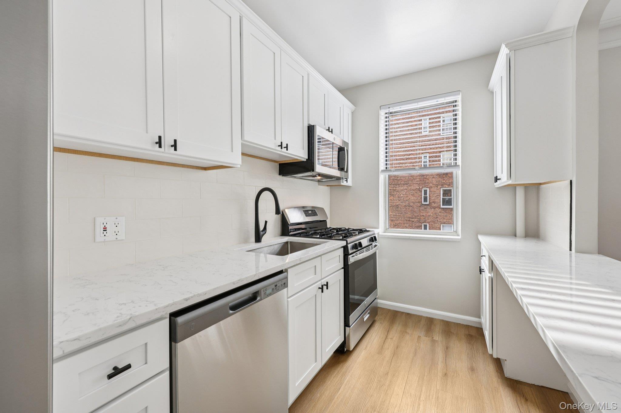1 Bronxville Road, Unit 3S Bronxville, NY 10708 - Photo 12 of 27 Kitchen with appliances with stainless steel finishes, light Quarts counters, white cabinetry, light wood finished floors, and backsplash
