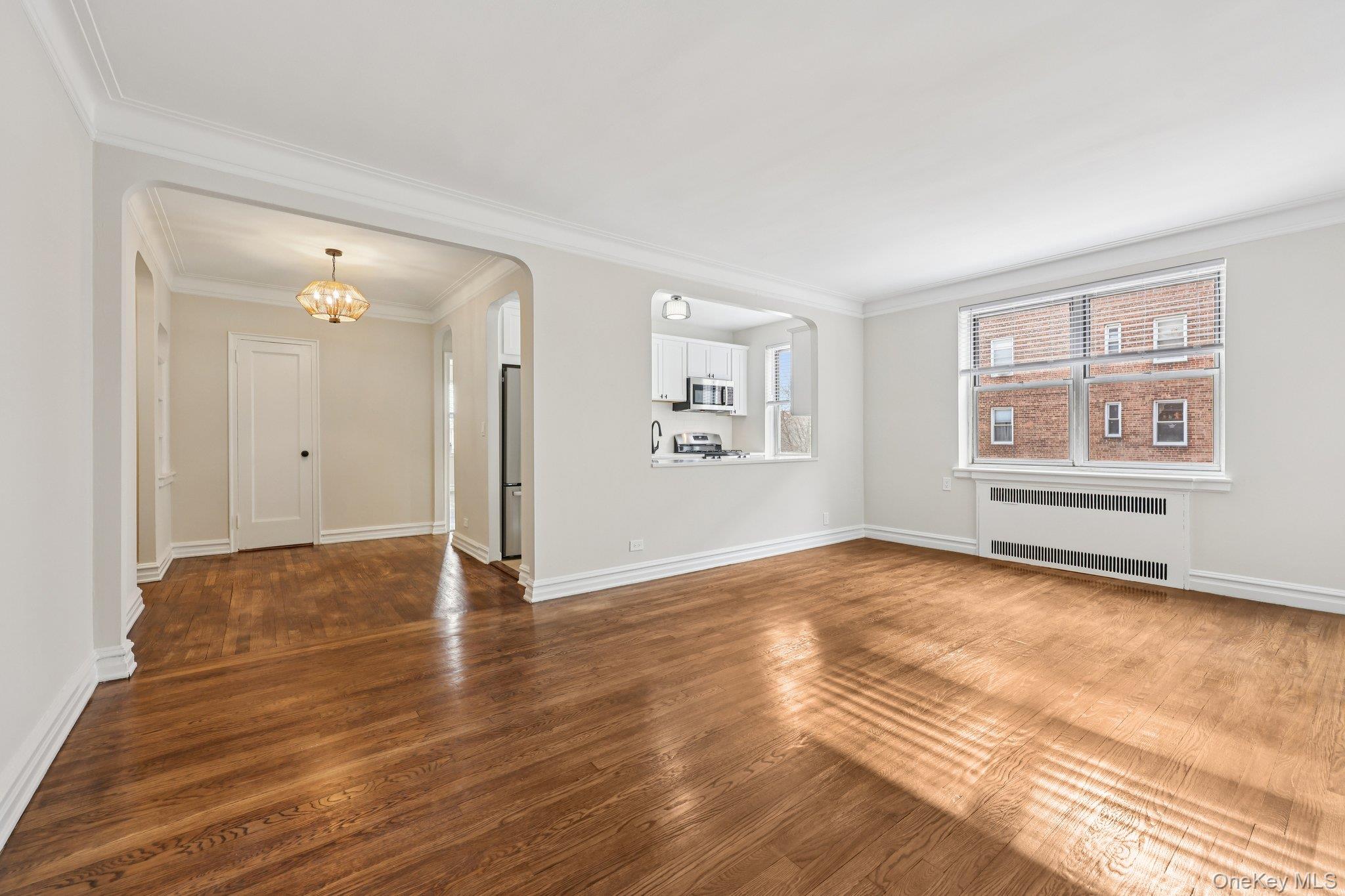 1 Bronxville Road, Unit 3S Bronxville, NY 10708 - Photo 10 of 27 Unfurnished living room with arched walkways, crown molding, radiator, dark wood finished floors, and a chandelier