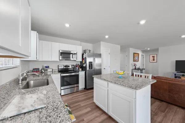 a kitchen with stainless steel appliances granite countertop a stove top oven a refrigerator a sink and dishwasher with wooden floor