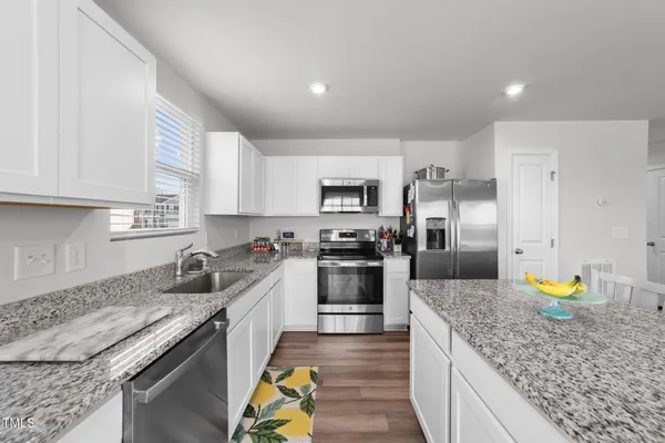 a kitchen with stainless steel appliances granite countertop a stove a sink a microwave a dining table and chairs with wooden floor