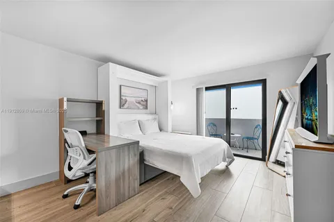 a bedroom with a bed a large window and a flat tv screen on dresser