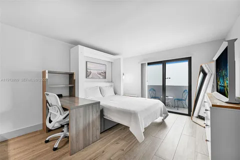 a bedroom with a bed a large window and a flat tv screen on dresser