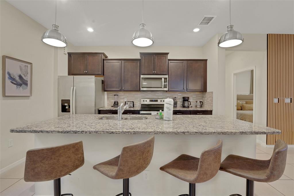 4450 Kaipo Road Davenport, FL 33897 - Photo 10 of 66 a kitchen with stainless steel appliances granite countertop a sink a stove a refrigerator cabinets and chairs