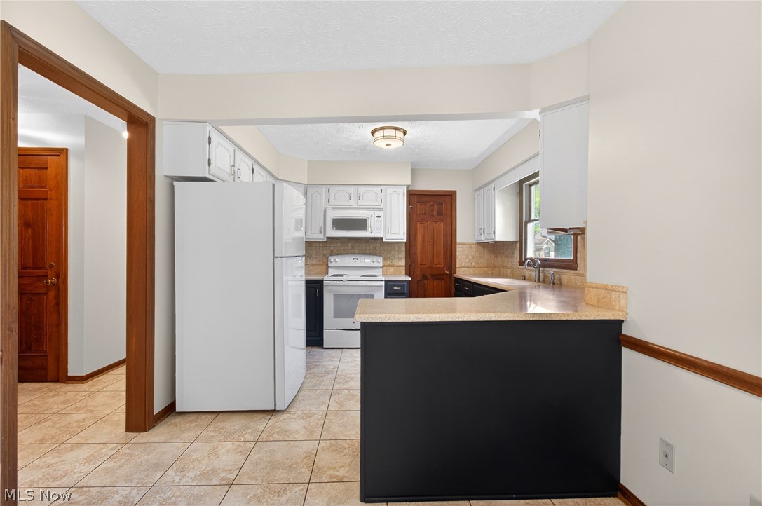 5346 Burlawn Street Northwest Canton, OH 44708 - Photo 10 of 40 Kitchen featuring white cabinetry, white appliances, a light-toned countertop, a tile backsplash, and tile flooring