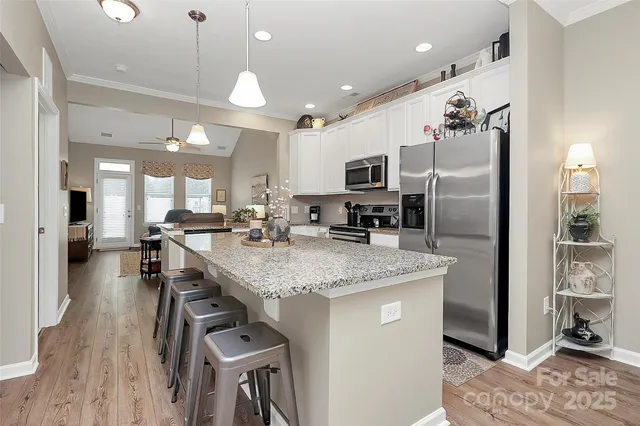 a kitchen with stainless steel appliances granite countertop a refrigerator a sink dishwasher a stove and a dining table with wooden floor