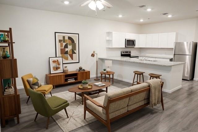 802 South 5th Street, Unit 1 Bonham, TX 75418 - Photo 5 of 25 Open-concept living area featuring wood-finish flooring, a contemporary kitchen with white cabinetry, stainless steel appliances, a breakfast bar, and recessed lighting