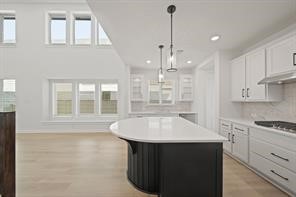 5423 Peach Gdn Way Manvel, TX 77578 - Photo 14 of 20 This photo showcases a modern kitchen with a spacious, open layout. It features a large island with a sleek countertop, pendant lighting, and ample natural light from multiple windows. The cabinetry is white, complemented by light wood flooring, creating a bright and airy atmosphere.