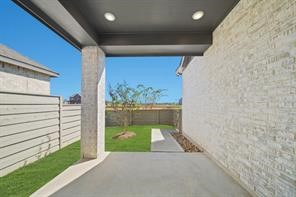 5423 Peach Gdn Way Manvel, TX 77578 - Photo 18 of 20 This photo showcases a covered patio area with recessed lighting and a view of a small, well-maintained backyard. The space is bordered by a modern horizontal fence and features a stone wall, offering a private and stylish outdoor area perfect for relaxation or entertaining.