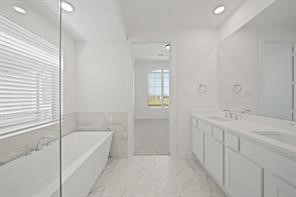 5423 Peach Gdn Way Manvel, TX 77578 - Photo 4 of 20 This bathroom features a clean, modern design with white cabinetry, a spacious bathtub, dual sinks, and ample natural light from a large window.