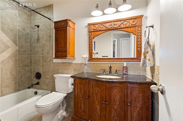 8135 Swan Road Colorado Springs, CO 80908 - Photo 14 of 16 Full bathroom with tile walls, tiled shower / bath, vanity, and toilet