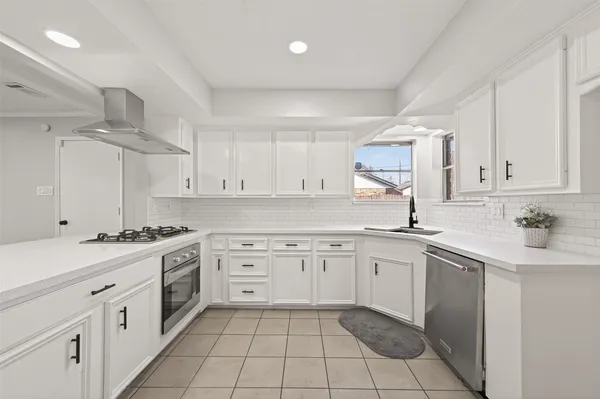 a kitchen with granite countertop a stove a sink dishwasher and white cabinets with wooden floor
