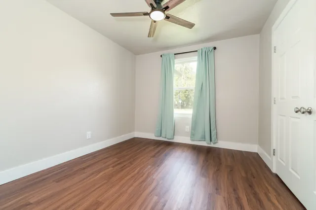 an empty room with wooden floor fan and windows