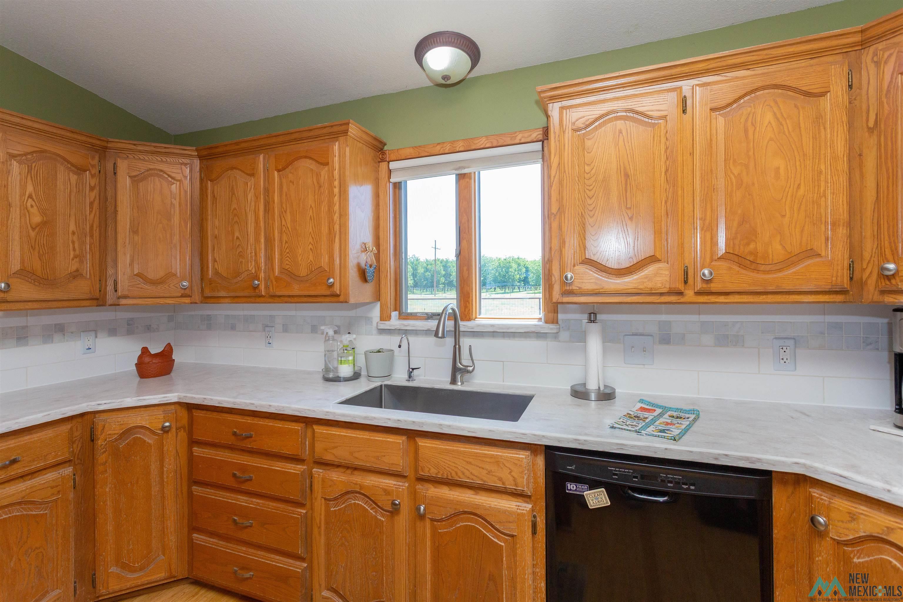 2012 South Haldeman Road Artesia, NM 88210 - Photo 22 of 96 Spacious kitchen featuring extensive wood cabinetry, light-toned countertops, a stainless steel sink with gooseneck faucet, a black dishwasher, and a window above the sink