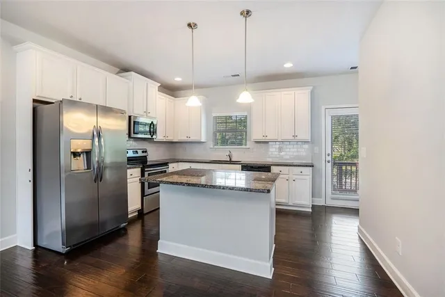 a kitchen with stainless steel appliances granite countertop a refrigerator a sink dishwasher a stove and white cabinets with wooden floor