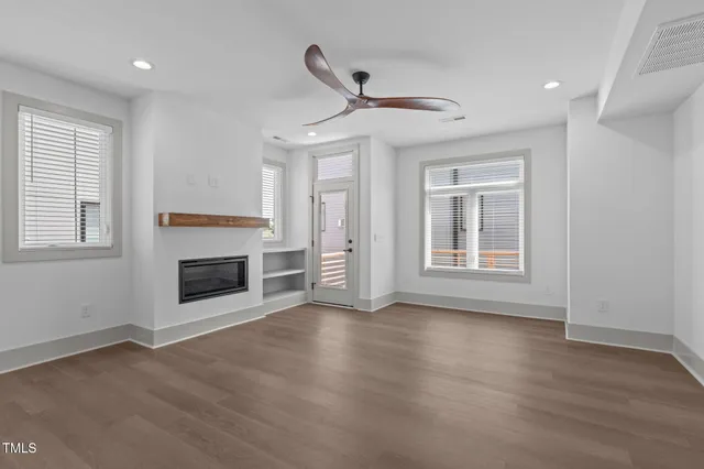 a view of an empty room with wooden floor fireplace and a window