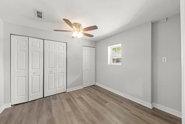 an empty room with wooden floor ceiling fan and windows