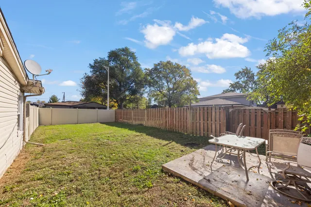 a view of backyard with table and chairs a fire pit and wooden fence