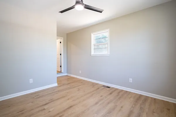 an empty room with wooden floor chandelier fan and windows