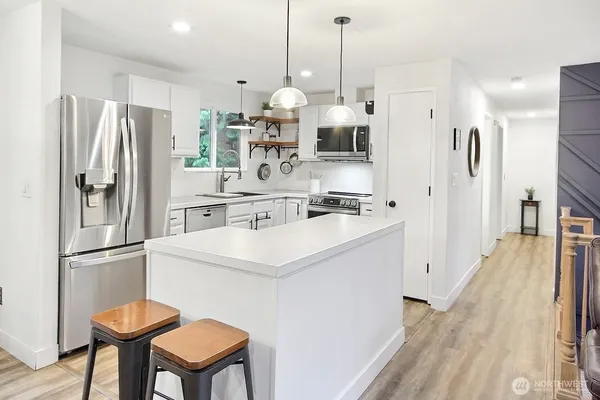 a kitchen with stainless steel appliances a refrigerator a sink dishwasher a stove and white cabinets with wooden floor