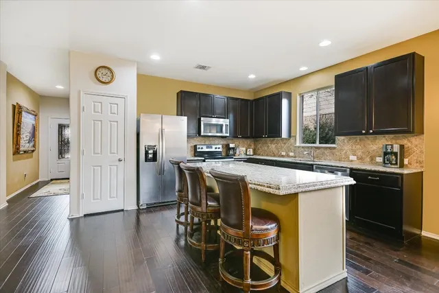 a kitchen with stainless steel appliances granite countertop a stove top oven a refrigerator a sink and a dining table with wooden floor